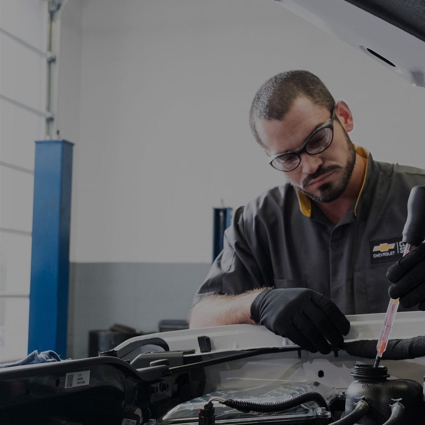 Chevrolet service technician in safety glasses checking fluid under the hood during an oil change