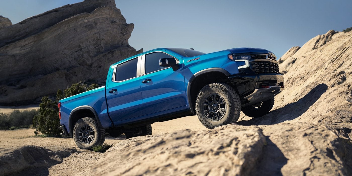 Blue Silverado 1500 crew cab climbing rocky desert terrain under a clear sky