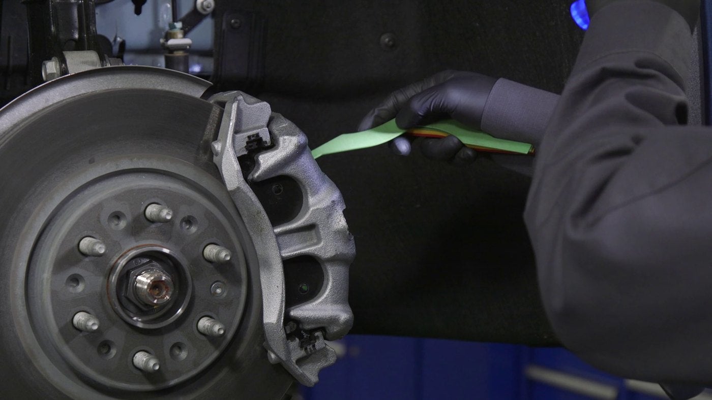 Close view of a Chevrolet brake rotor and caliper with a technician measuring pad thickness