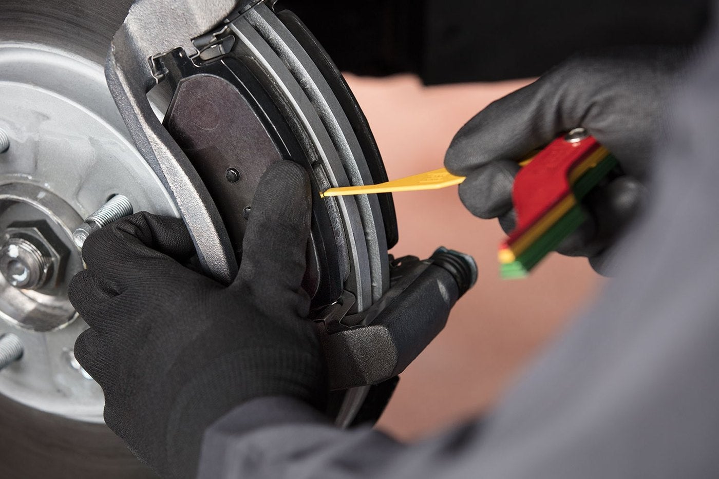 Technician holding a brake pad wear gauge against a Chevrolet brake pad during brake service