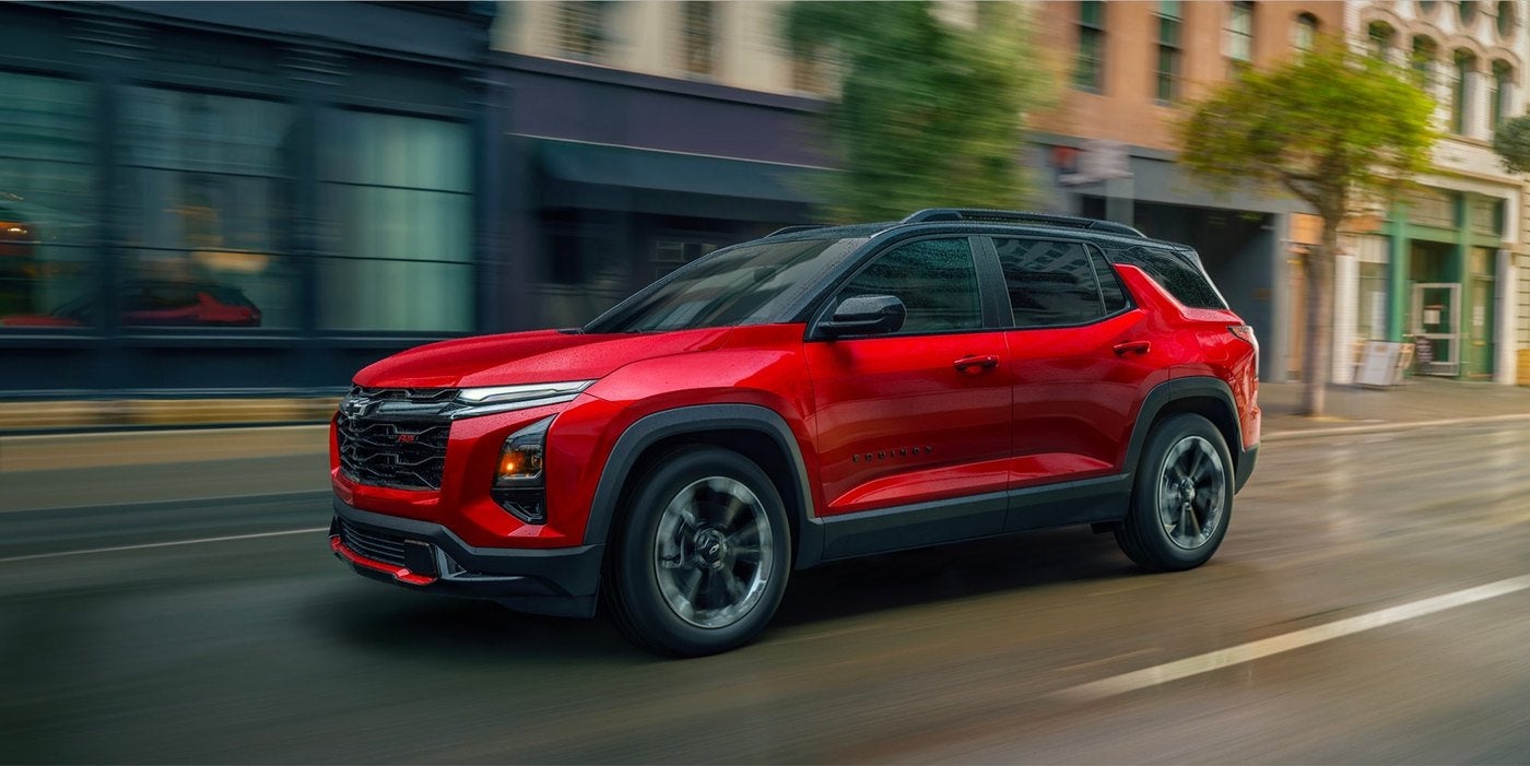 Red Chevrolet Equinox driving down a city street with shops in the background