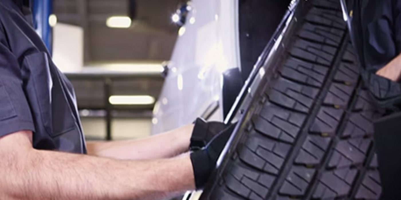 Chevrolet service technician holding a tire on a lift to inspect the tread during tire rotation