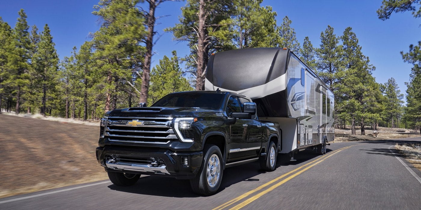 Black Silverado HD towing a fifth wheel camper down a tree lined road