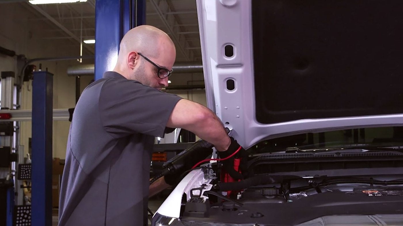 Service technician connecting jumper cables to a battery under a raised hood