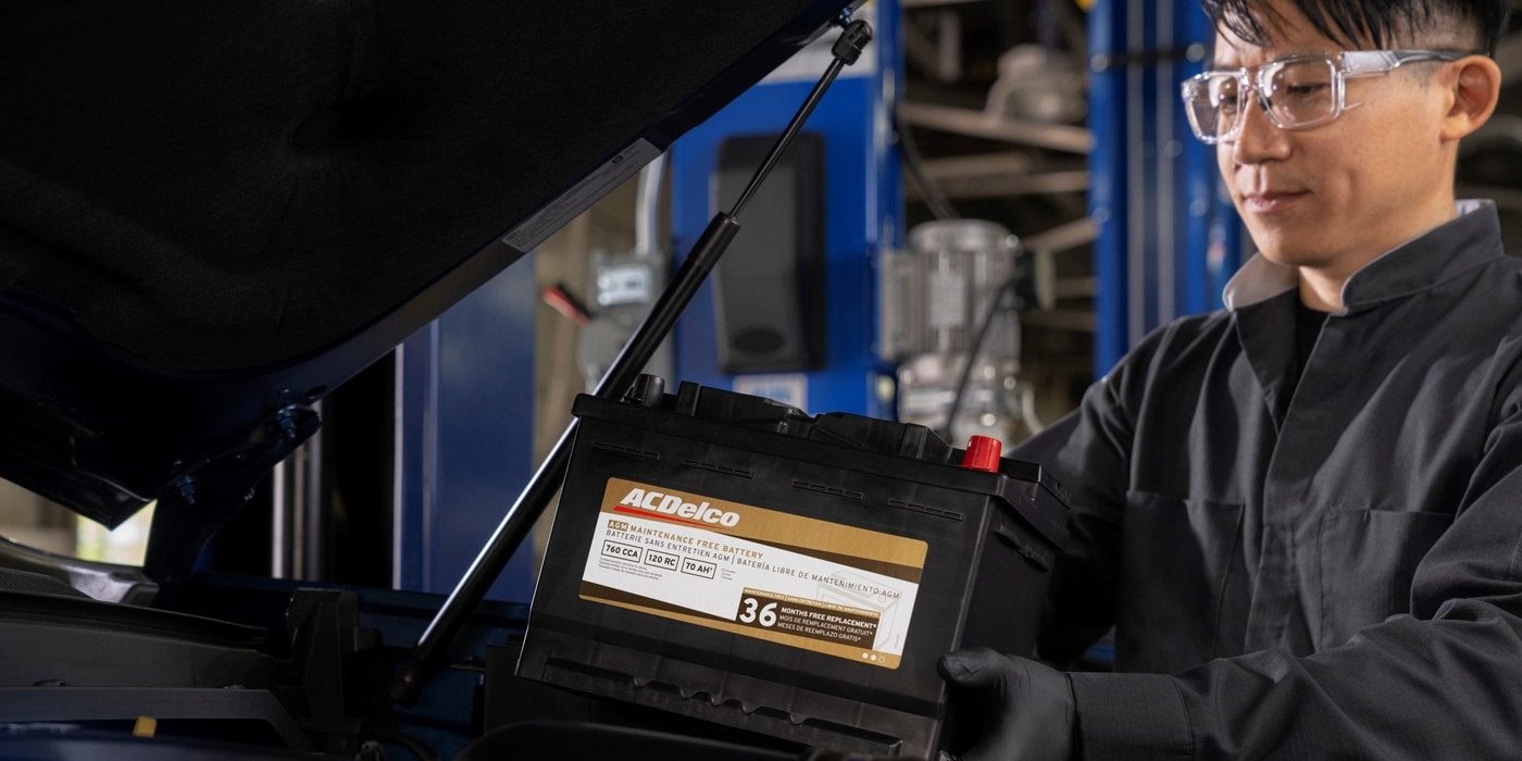 Chevrolet technician in safety glasses lowering a new ACDelco battery into a vehicle