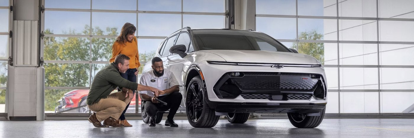 Service advisor and customers crouched beside a Chevrolet electric SUV in a service bay