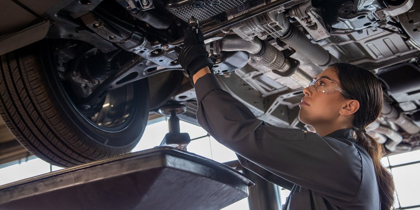 Chevrolet technician in safety glasses inspecting the underside of a vehicle on a lift