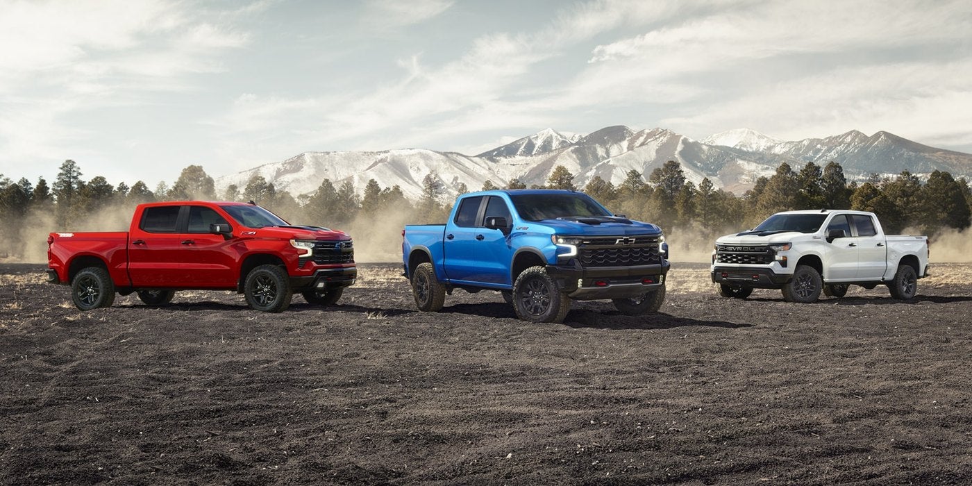Red, blue and white Silverado 1500 trucks parked side by side in a field