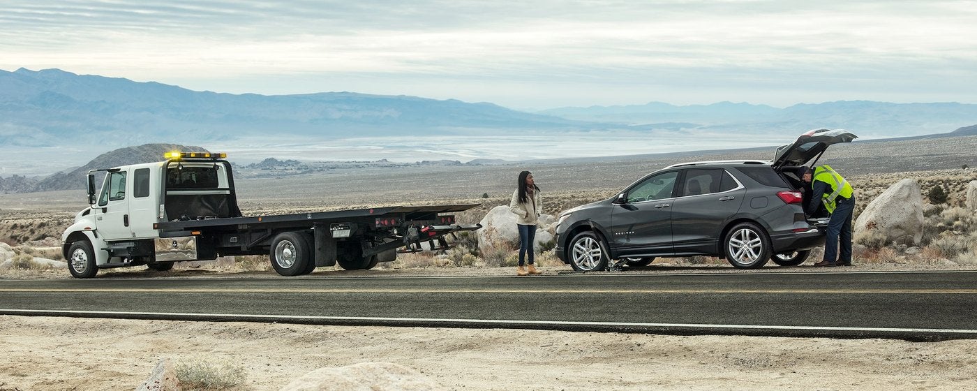 Flatbed tow truck on a desert highway with a Chevrolet Equinox and two people beside it