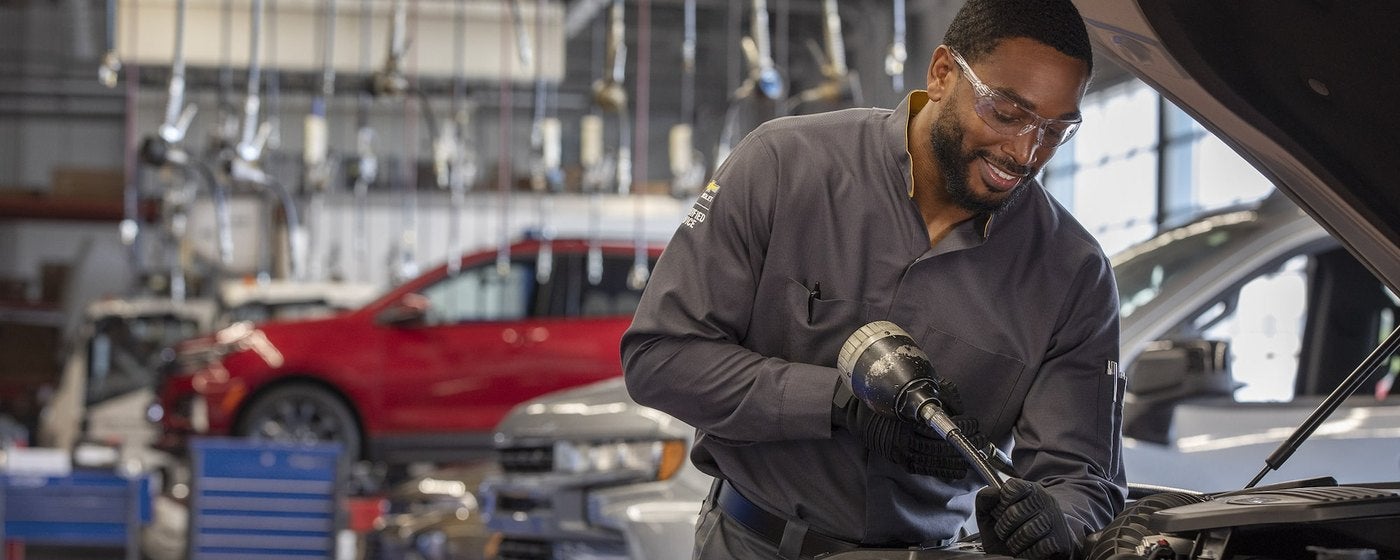 Smiling Chevrolet technician using a tool under the hood in a busy service shop