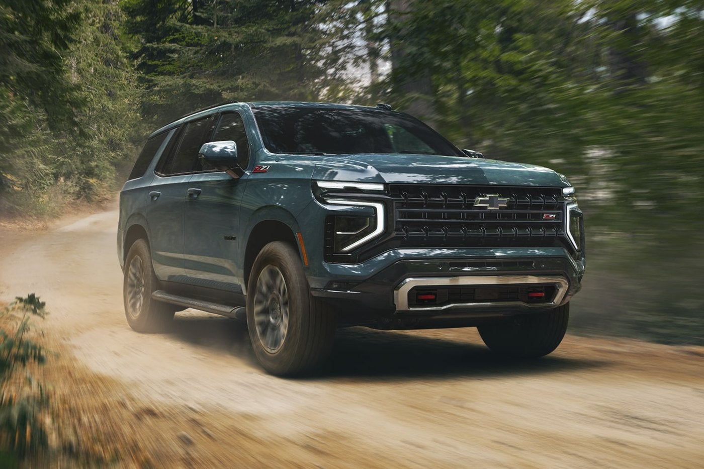 Dark teal Chevrolet Tahoe driving fast on a forest dirt road