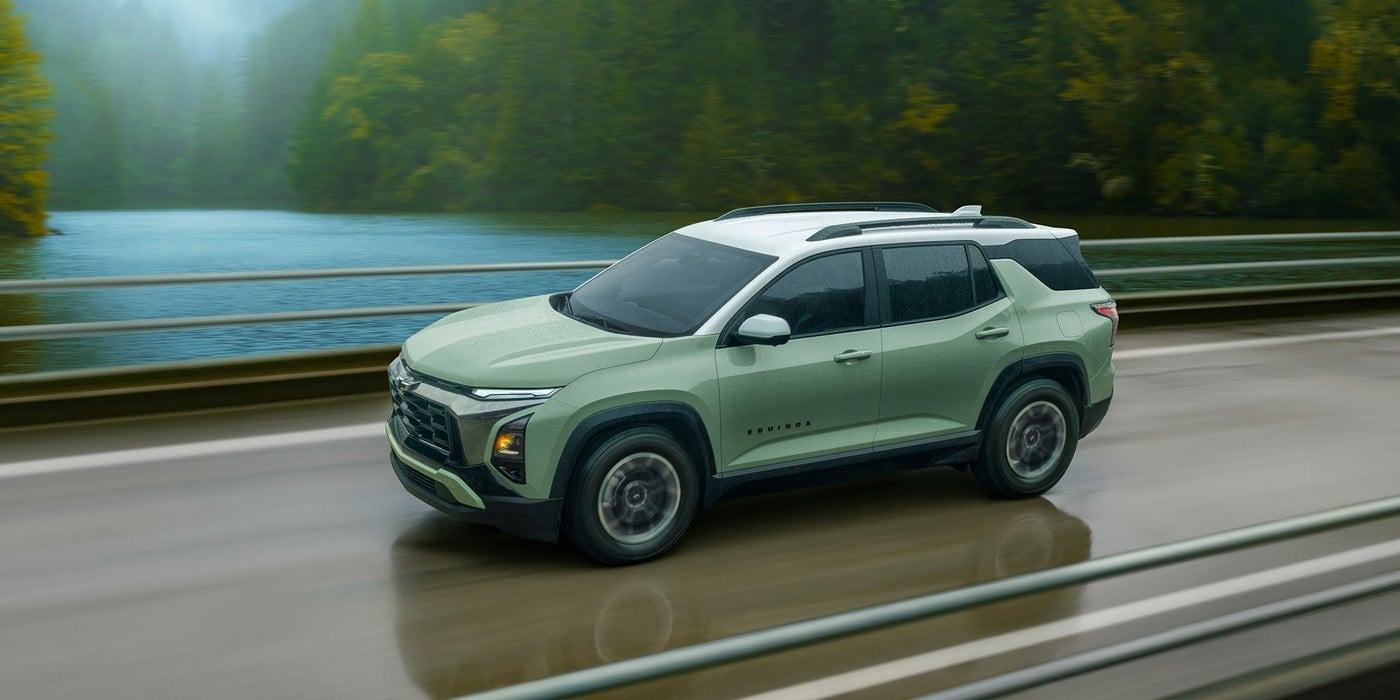 Green Chevrolet Equinox driving on a road beside a forest river