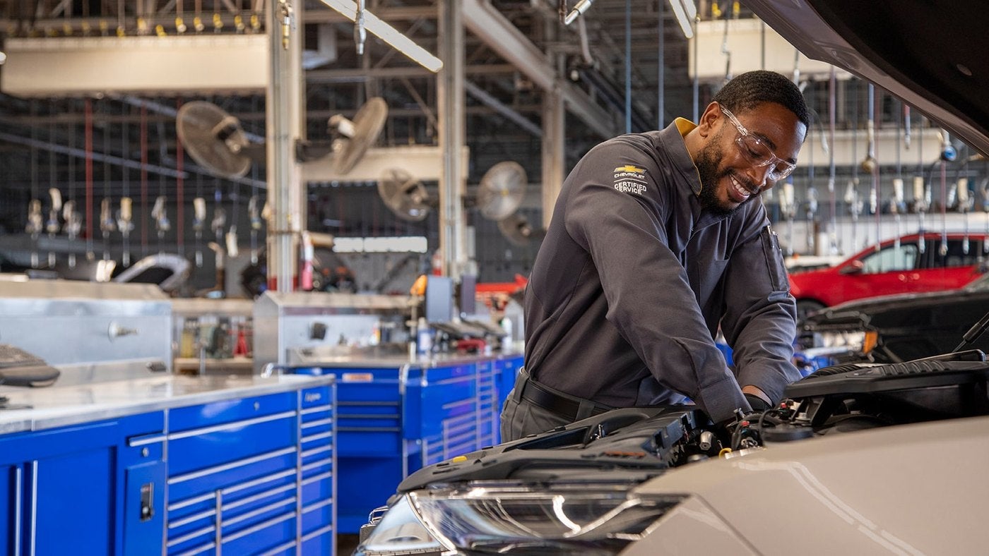 Chevrolet technician leaning into an engine bay in a service shop