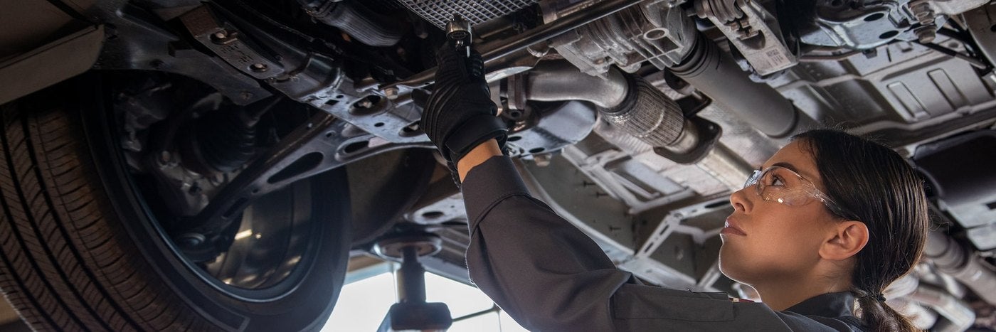 Chevrolet technician reaching up to inspect the exhaust and underbody of a lifted vehicle