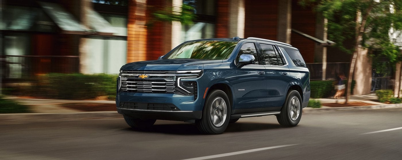 Blue Chevrolet Tahoe driving down a tree lined city street